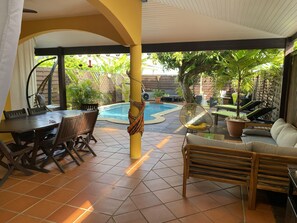 Terrasse, coin détente, piscine et salon au fond du jardin sous le manguier