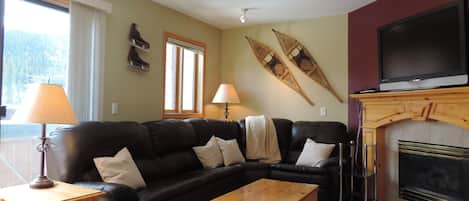 Living room with leather sectional couch, gas fireplace, & TV.