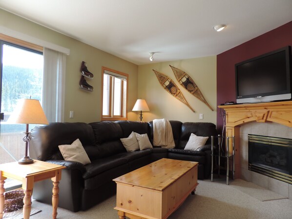 Living room with leather sectional couch, gas fireplace, & TV.