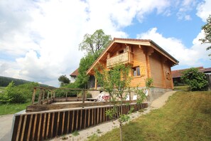 La grande terrasse devant le chalet , avec une table , barbecue et transats