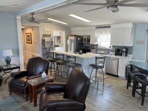 Open floor plan shows two living room recliners, kitchen and dining room table.