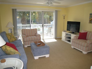 Living room with LCD TV and covered balcony overlooking tropical palms and pool 