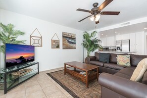Vantage point from the unit's entry area toward kitchen, living room and TV. Ceiling fans and tile flooring throughout living areas.
                