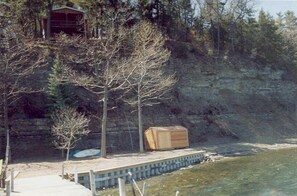 The partial view of lakefront and dock with cottage perched above