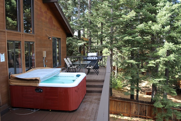 Back deck with a large Hot Tub, table with chairs and a BBQ