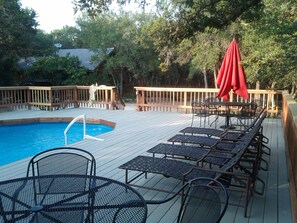 Pool has several lawn chairs and tables for lounging.