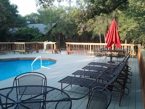 Pool has several lawn chairs and tables for lounging.