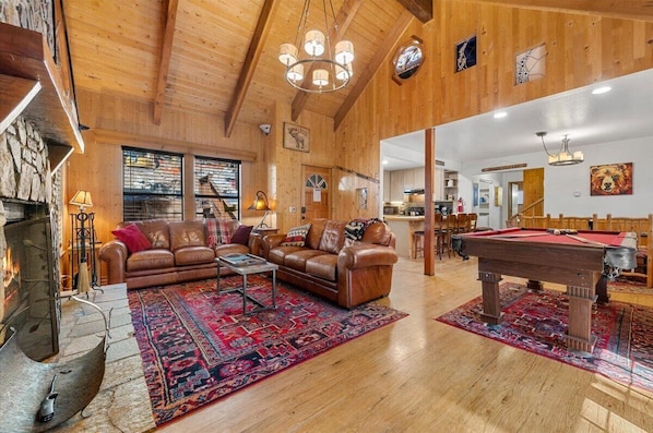 2 leather couches face the fireplace with beamed ceilings and knotty pine.