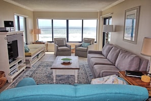 Living room has flat screen TV, views of the ocean, and two swivel chairs.