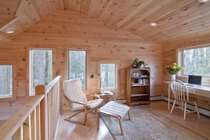 Reading + work space in loft surrounded by picture windows with forest views