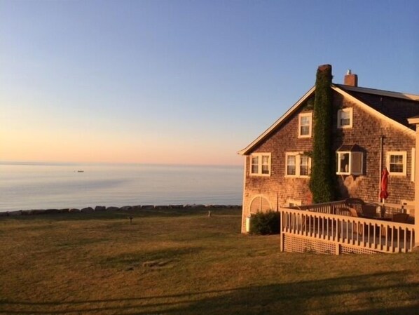 View of house and deck with expansive lawn area with seawall and beach.