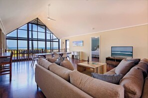 Relax in the open-plan upstairs living area, featuring vaulted ceilings, plush seating, and panoramic windows that frame the Indian Ocean.