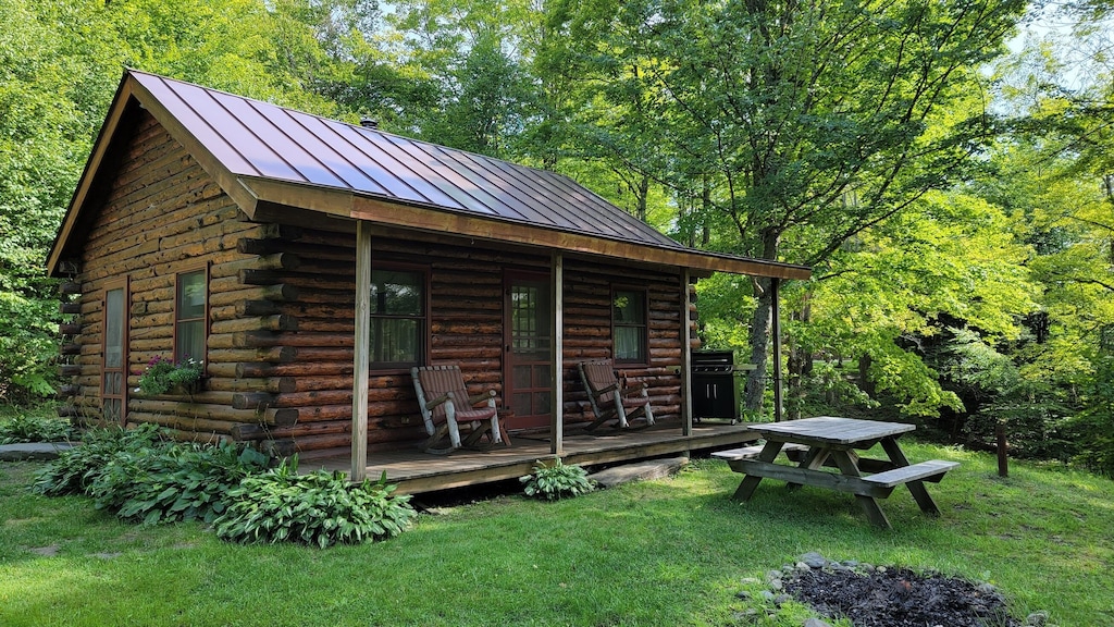 A classic Vermont log cabin seen with bright green trees and grass all around