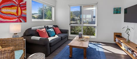 Comfortable lounge area with large smart TV and blinds on windows.