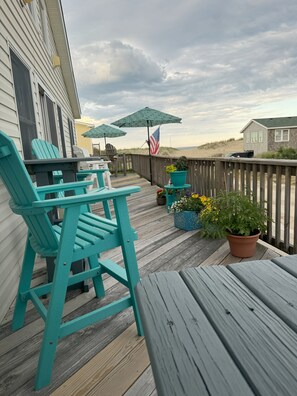 Long front porch with 7 counter chairs,  2 tables, a picnic table & 3 umbrellas.