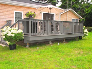Back yard with large deck ,couch,  dining table and gas grill and grassy yard.