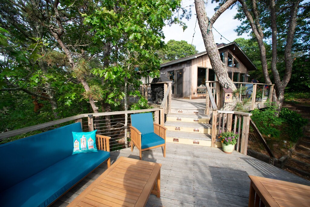 A Massachusetts treehouse rental with a roomy outdoor living space with couches, chairs, and tables is nestled in the trees