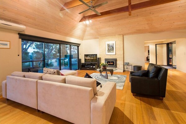 The spacious open-plan living area features high cathedral ceilings, timber floors, and floor-to-ceiling windows that fill the home with natural light and tranquil views.