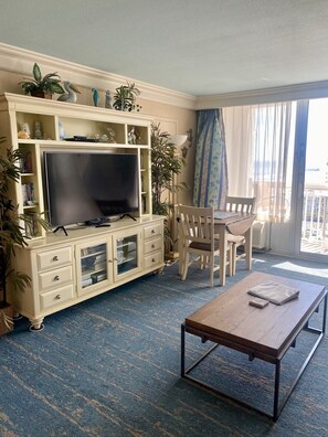 Modern living room with large flatscreen TV, tables, and chairs