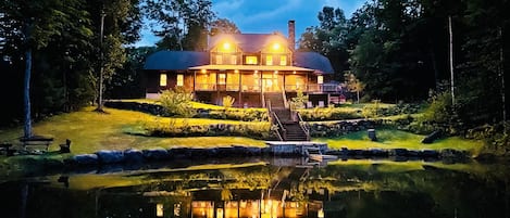 A lovely view of the back of cabin, firepit, and pond at dusk. 