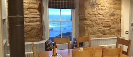 The kitchen with dining table looking out to the water with log burner.