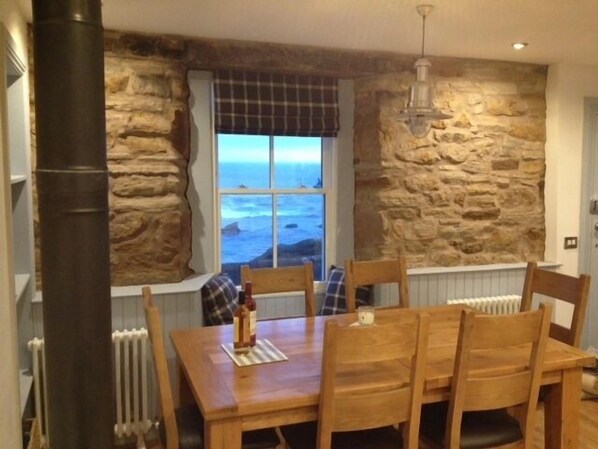 The kitchen with dining table looking out to the water with log burner.