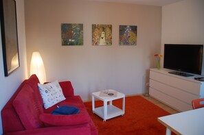 Das Wohnzimmer mit Sofa, Fernseher und Schreibtisch
