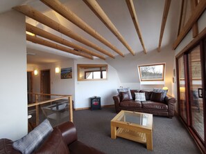 Upstairs seating area with double height ceiling and beams. 2 leather settees.