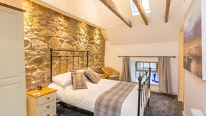 Masterbedroom, original stone wall and timber beams softened with tweeds