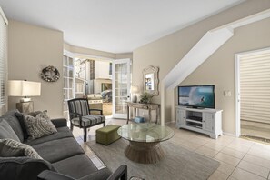 Vantage point from dining table and seating toward living room, TV, entry door and front French doors out to patio. Tile flooring throughout living spaces.
                