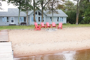 Looking at the home from dock.  Adirondack chairs around firepit on the beach.