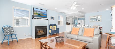 The main living area includes TV, fireplace, leather sofa with queen pullout bed, dining table with seating for 6, and doors that lead to the ocean view patio.