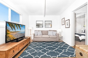 The main living area includes a couch, cable TV, dining table with seating for four, and a direct bay view.
                