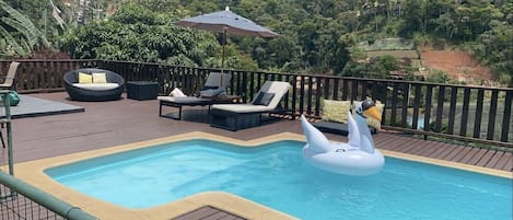 Linda piscina privativa com espreguiçadeiras, guarda sol e mesinha para bebidas.