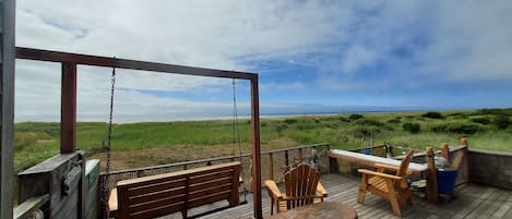 Large oceanside deck with porch swing, dining table, hammock chair and bbq grill