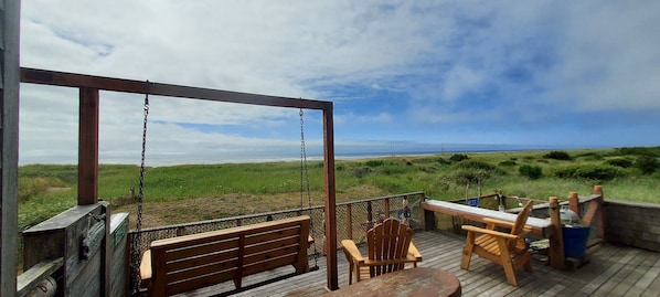 Large oceanside deck with porch swing, dining table, hammock chair and bbq grill