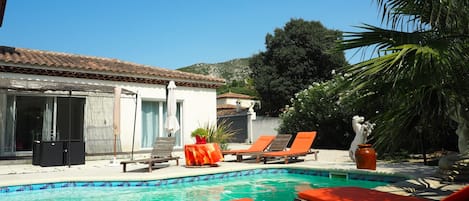 Vue de la terrasse privée ombragée donnant sur la piscine et les transats.