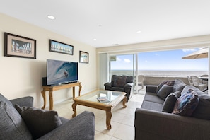 The living area includes cable TV, sofa set, and sliding glass doors to the oceanfront patio.
