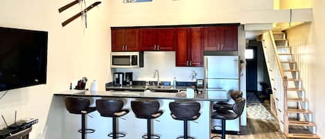 Kitchen, barstools, large TV and stairs that lead to two small bedrooms upstairs