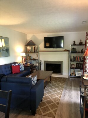 Open floor plan living room with modest couch, 50 inch flat screen , fireplace.