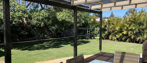 Large grassy back yard with undercover deck, bbq and kids play equipment