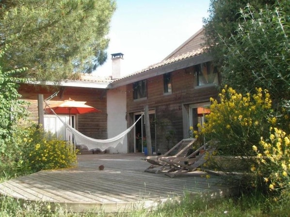 Vue d'ensemble de la maison depuis le jardin, avec la terrasse en premier plan