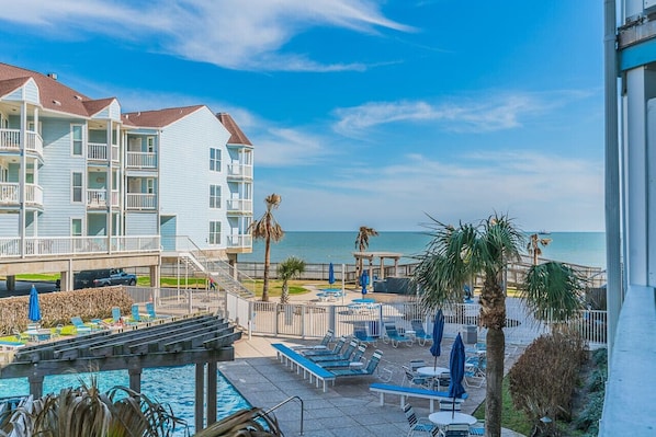 A luxurious resort with a sparkling pool overlooking the ocean, surrounded by lush greenery and palm trees, set against a backdrop of Gulf of Mexico.