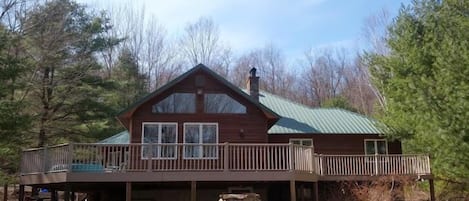 Front View, Large Deck, Patio Area with stone fire pit and charcoal grill.