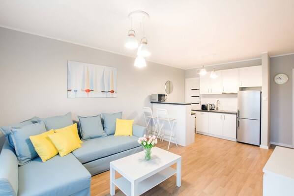 A bright living room with a comfortable blue and yellow sofa, a wooden coffee table, and a small dining area in the background, creating a cozy and welcoming atmosphere.