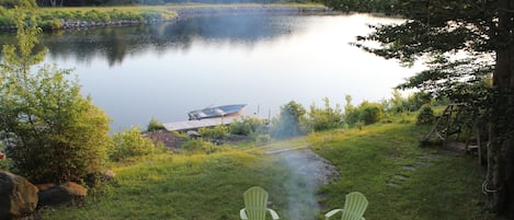 Lakefront private view from deck with boat, dock, fire pit, and swing. 