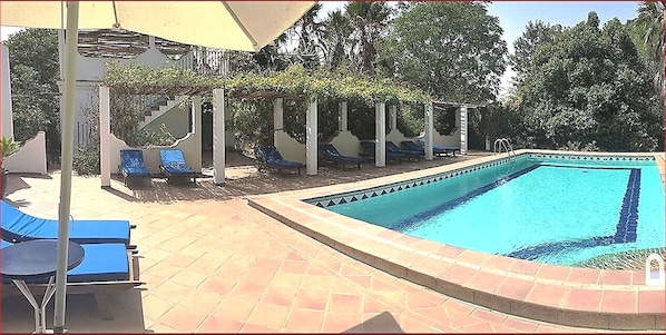 The pool, surrounded by partly shaded terraces  with sunbeds.