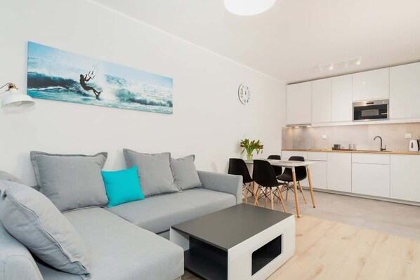 A cozy, open-plan living room with a sofa, wall-mounted TV, and decor in soft shades, with turquoise accents for added vibrancy.