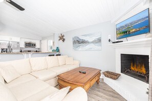 The living area includes sofa, cable TV,  dining table with seating for 6, and kitchen beyond.
                