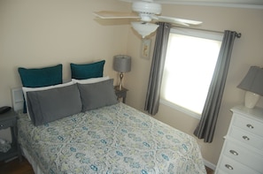 Bedroom has a ceiling fan and window with shades and curtains.